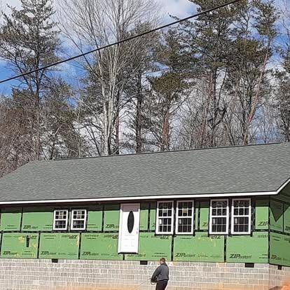 Green house under construction with white front door, a person standing outside, and trees overhead