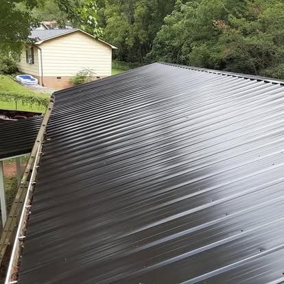 Black metal roof on a house, with trees and a small beige shed in the background.