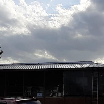 Cloudy sky over a long dark-roofed building with a ladder on the right and chairs on the porch.