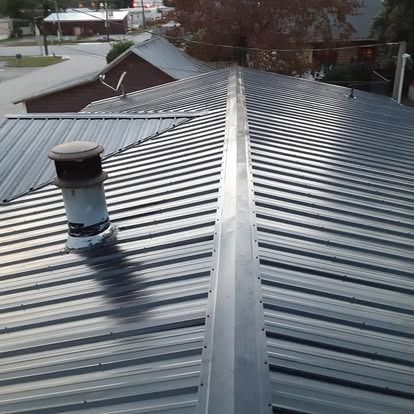 Metal roof with a central ridge vent and a chimney under a cloudy sky.