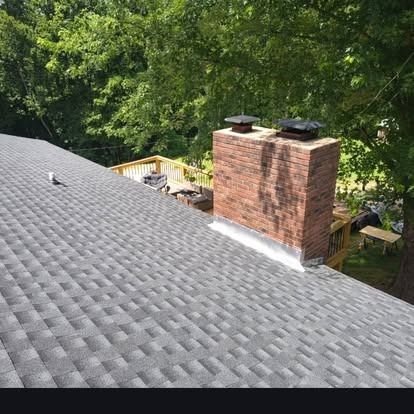 Gray shingled roof with brick chimney and trees in the background