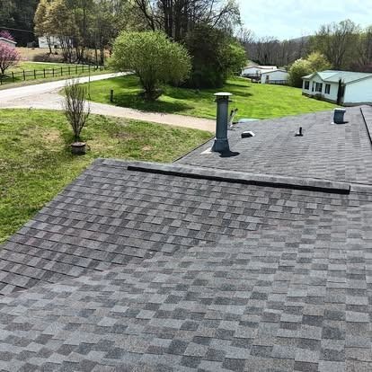 Rooftop with gray shingles, chimney, and vents overlooking a green yard and road on a sunny day
