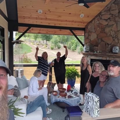 Friends smiling and posing on a covered patio with stone walls and wood ceiling, with drinks and table decor