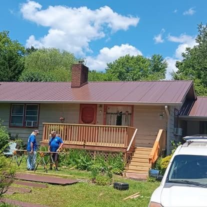 Workers repairing a porch on a beige house with a brown roof, under a blue sky.