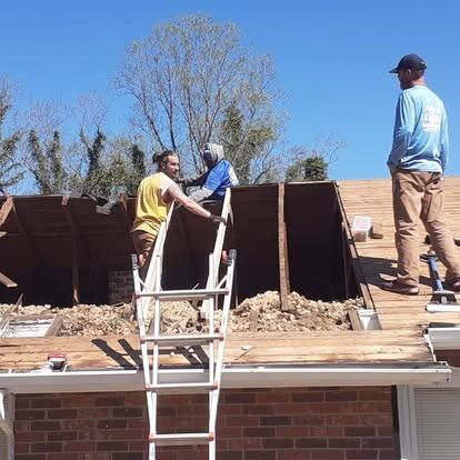 Workers repairing a rooftop beside a ladder under a clear blue sky