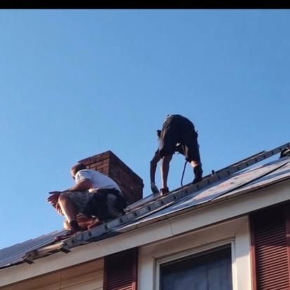 Two workers repairing a gray shingled roof under a clear blue sky