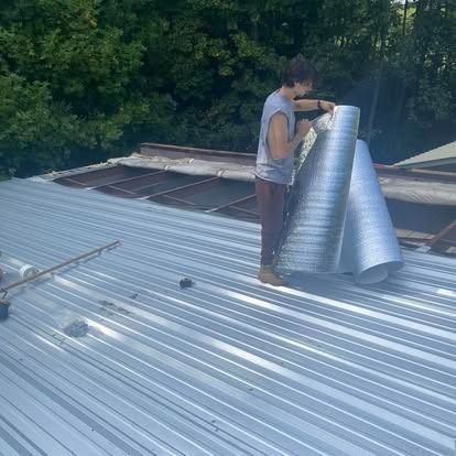 Worker installing silver roofing panels on a corrugated metal roof outdoors