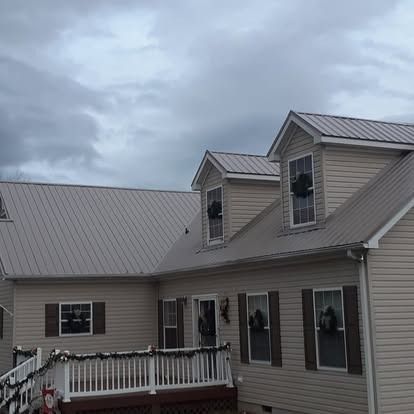 Suburban house with gray siding, dormer windows, and a white-railed deck under a cloudy sky