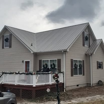 Suburban house with gray siding and metal roof, white deck, and overcast sky
