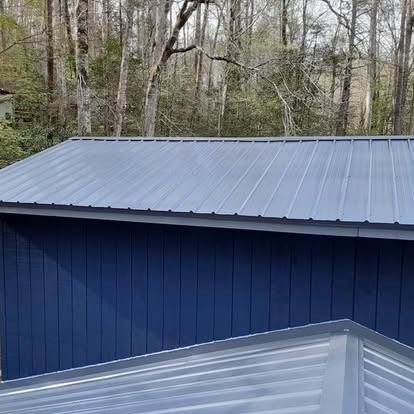 Blue metal-roofed building beside trees, with a gray roof in the foreground