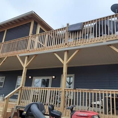 Two-story dark house with a wooden balcony and porch, with a red lawn tractor parked in front.