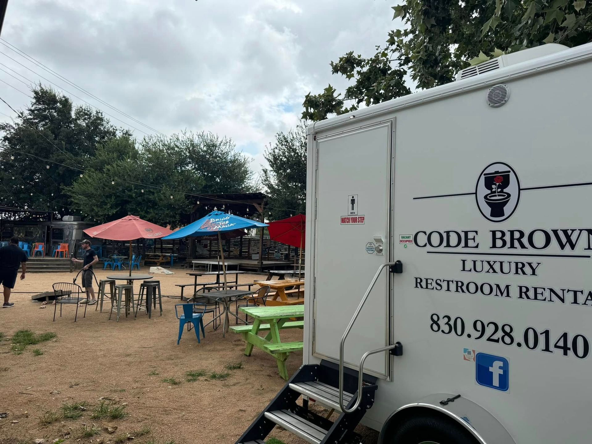 Outdoor event area with tents, tables, and a white Code Brown luxury restroom trailer