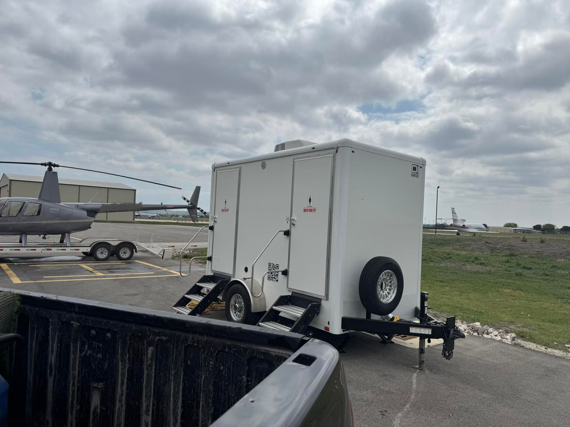 White utility trailer near a helicopter on an airfield under cloudy skies