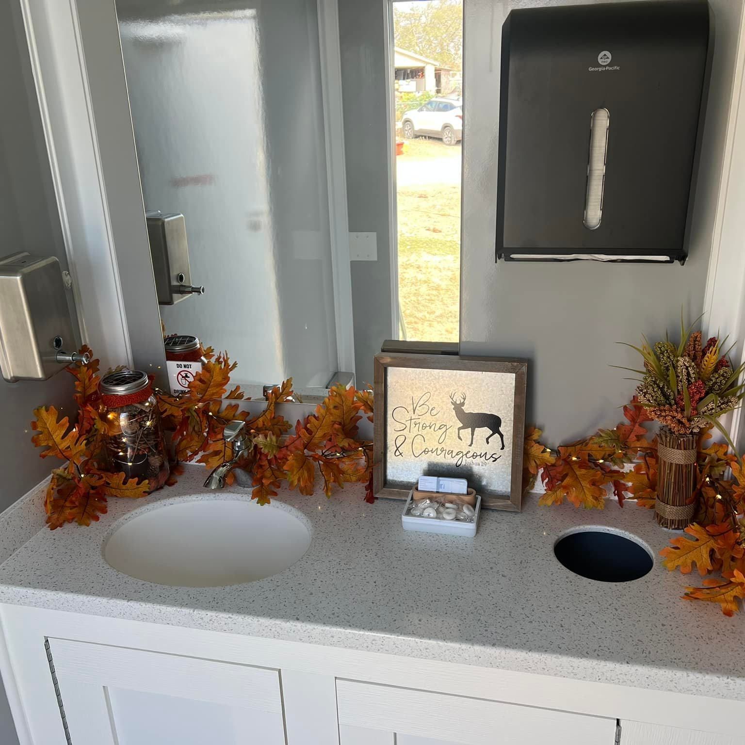 Decorated restroom counter with autumn leaves, deer sign, sinks, and paper towel dispenser