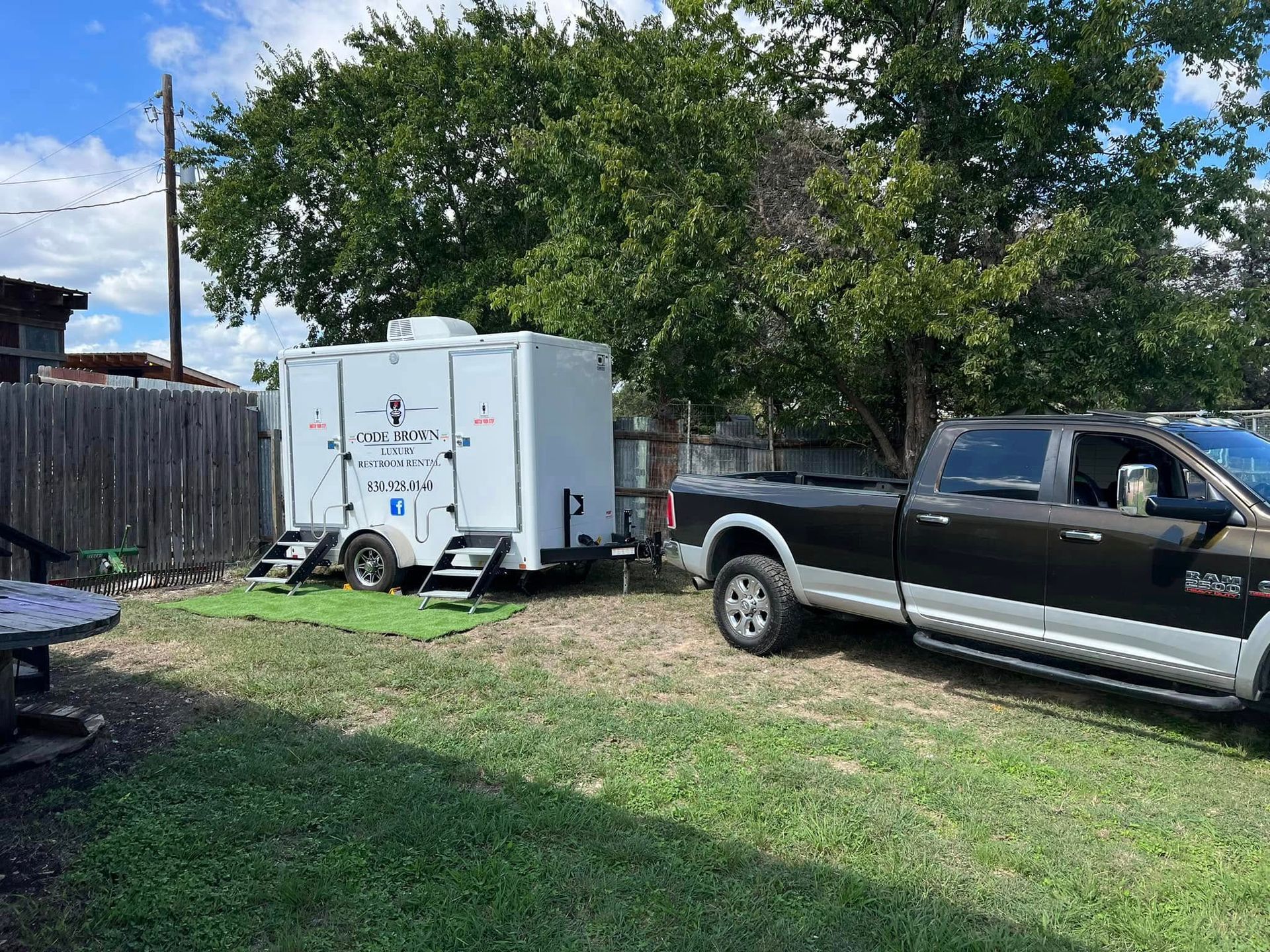 Backyard with a white trailer and black pickup truck beside a wooden fence and trees.