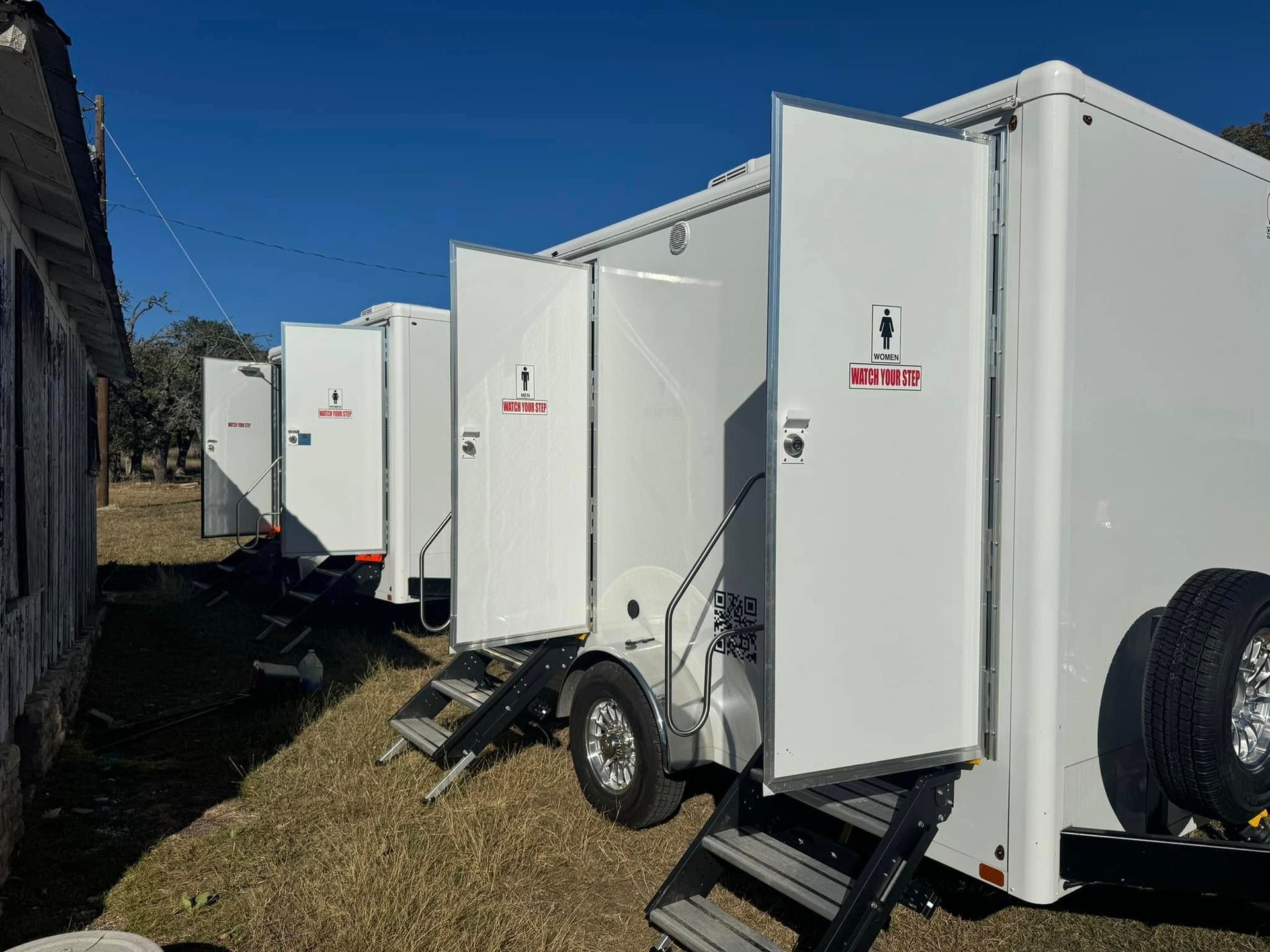 Row of white portable restroom trailers parked on grass under a blue sky