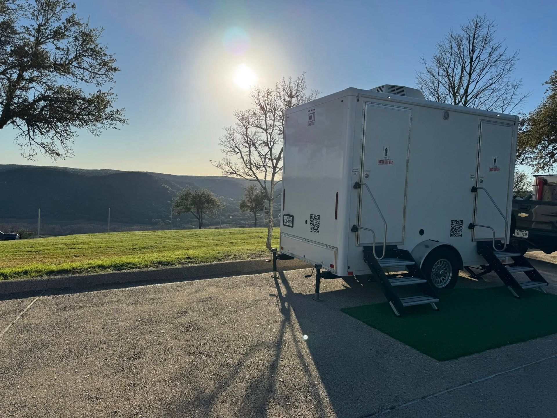 White trailer on a gravel lot beside a road, with the sun low over distant hills.