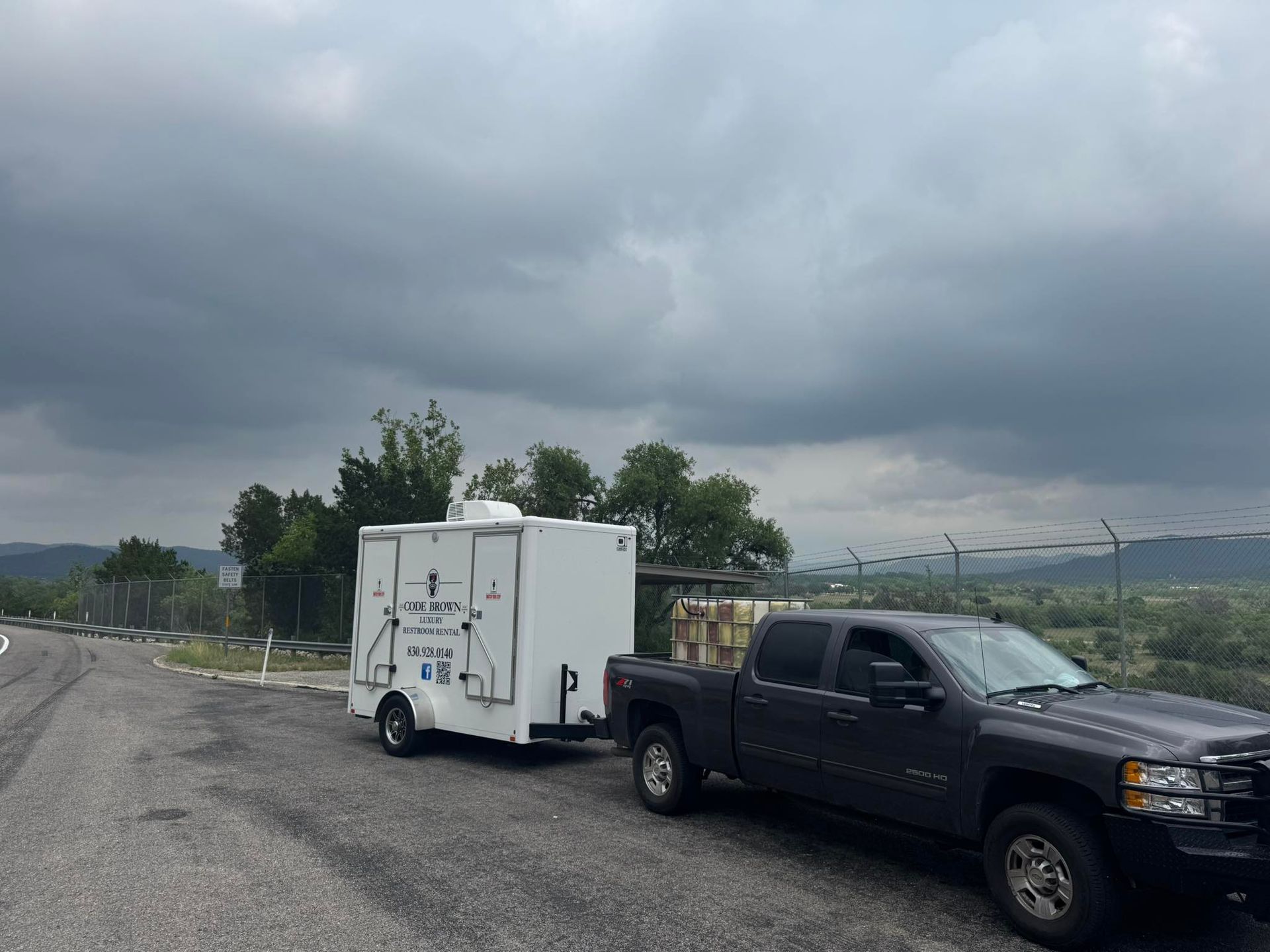 Black pickup truck towing a white trailer on a road under cloudy skies
