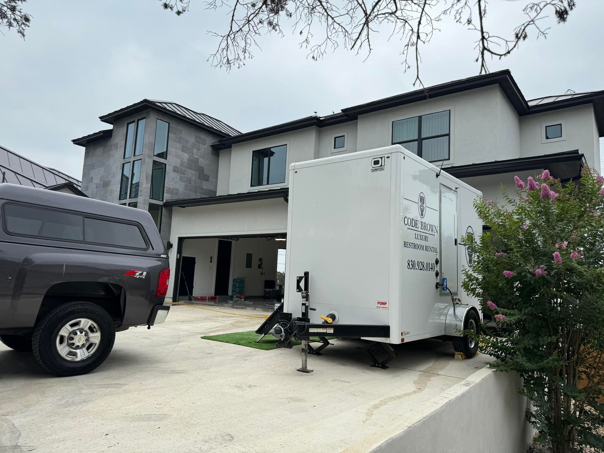 White box truck and black pickup in a driveway beside a modern two-story house.