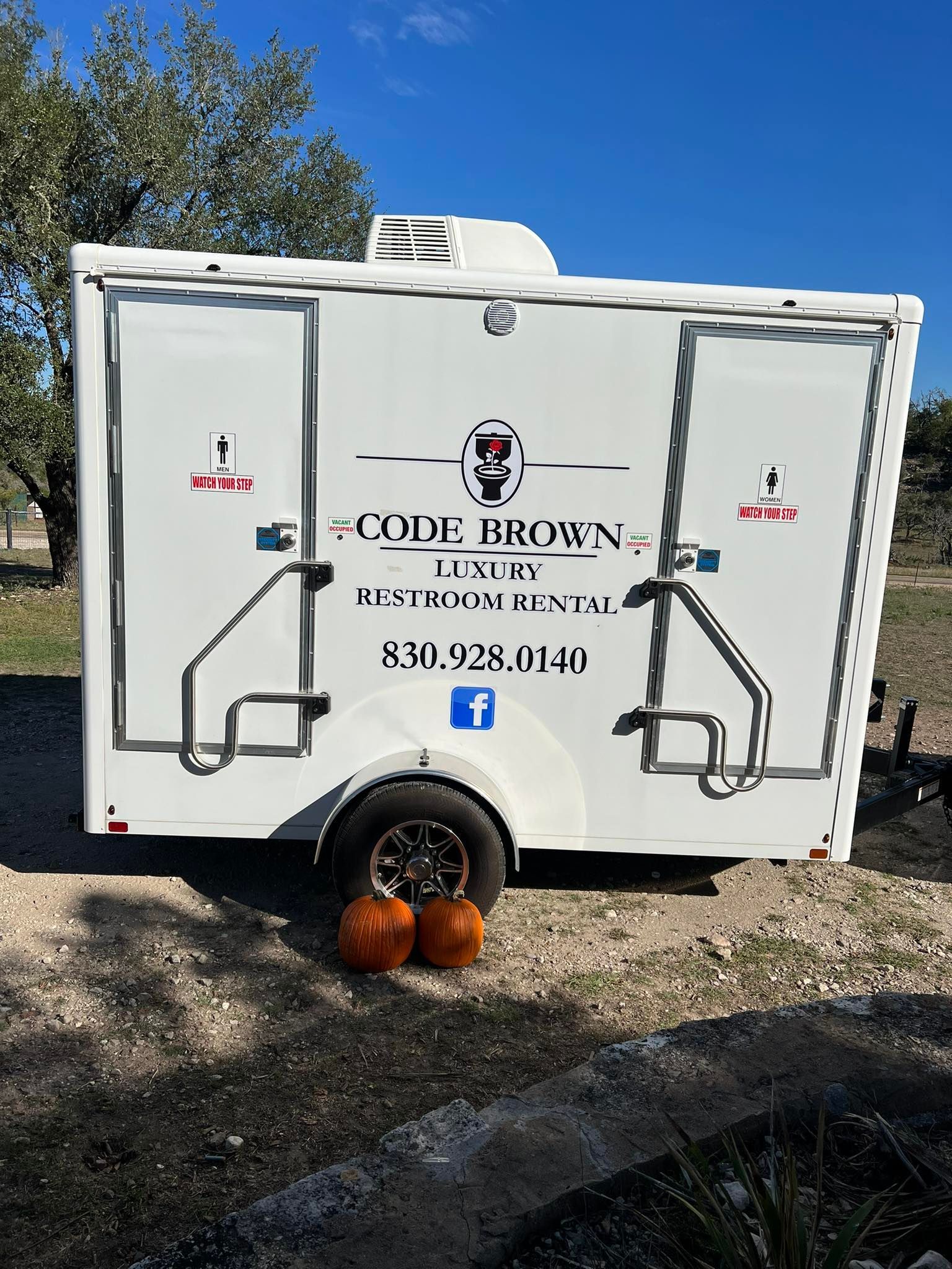 White food truck trailer with logo parked outdoors, pumpkins by the wheels and trees in the background