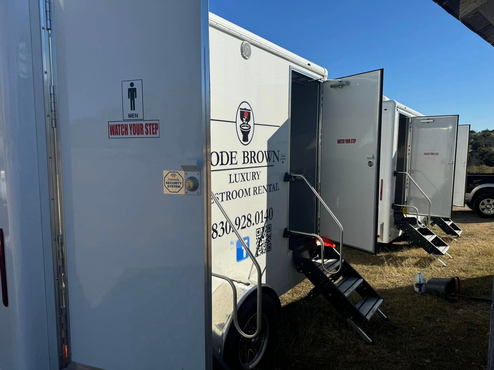 White trailers lined up outdoors with a small stairway and a sign on the nearest trailer.