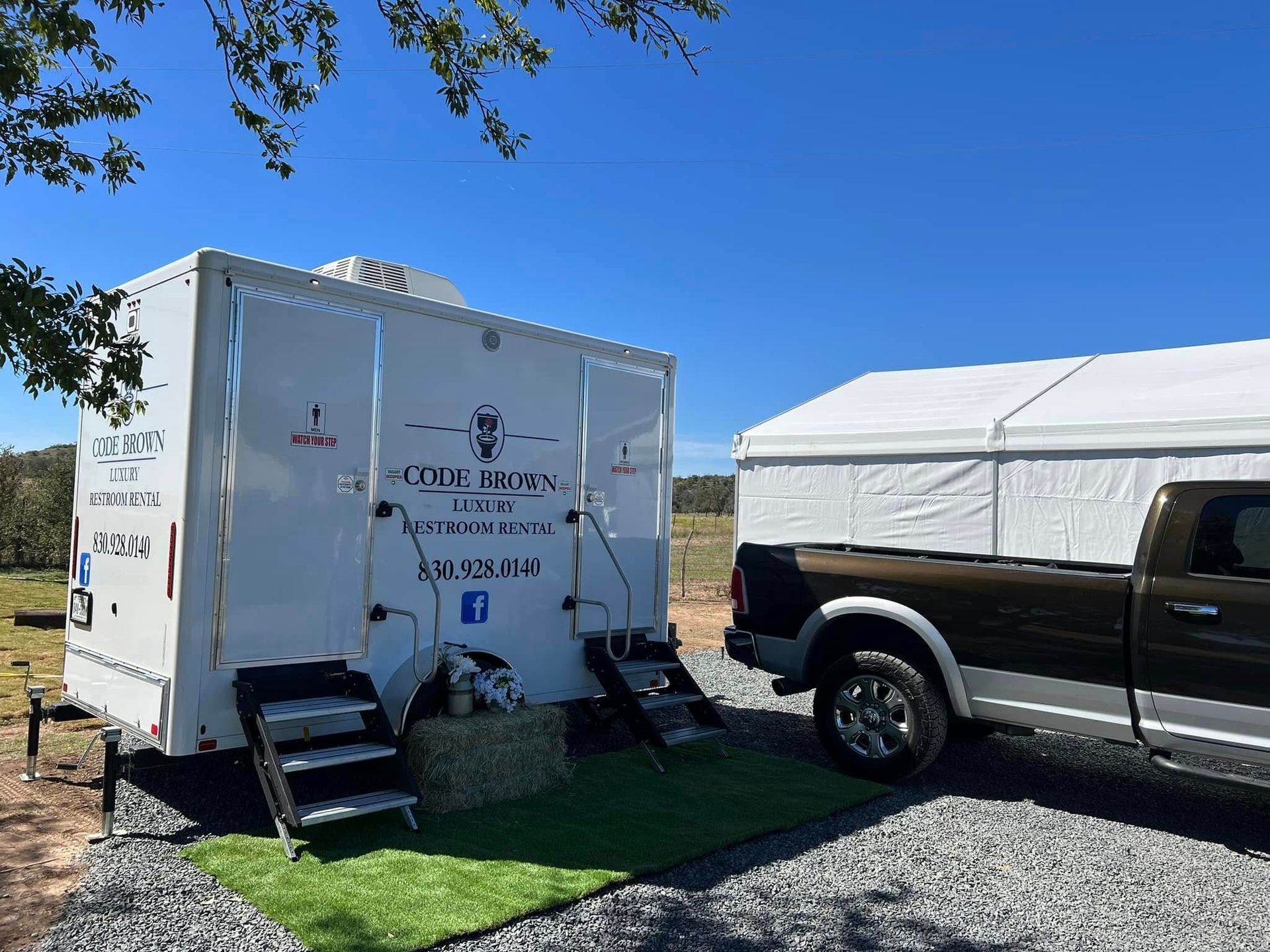 White horse trailer and black SUV parked on grass under a clear blue sky.