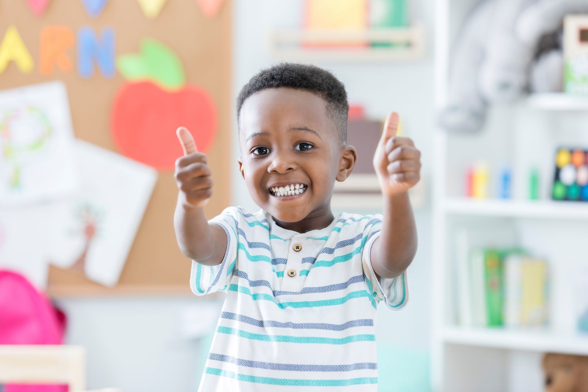 A young boy is giving two thumbs up in a classroom.