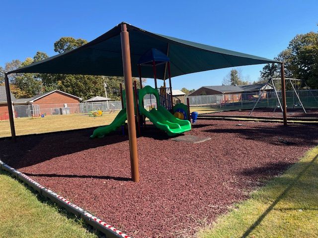 A playground with a green slide and a green shade.