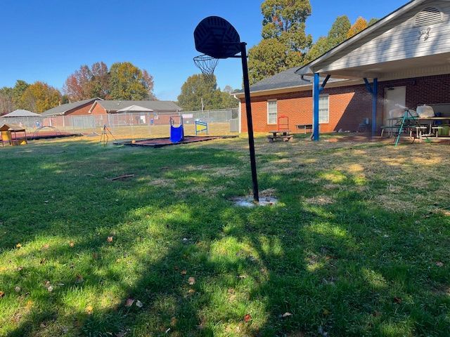 A basketball hoop is in the grass in front of a house.