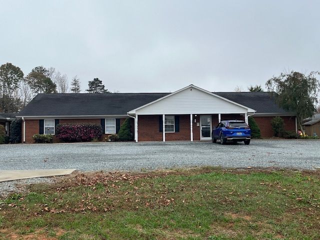 A blue car is parked in front of a large brick house.