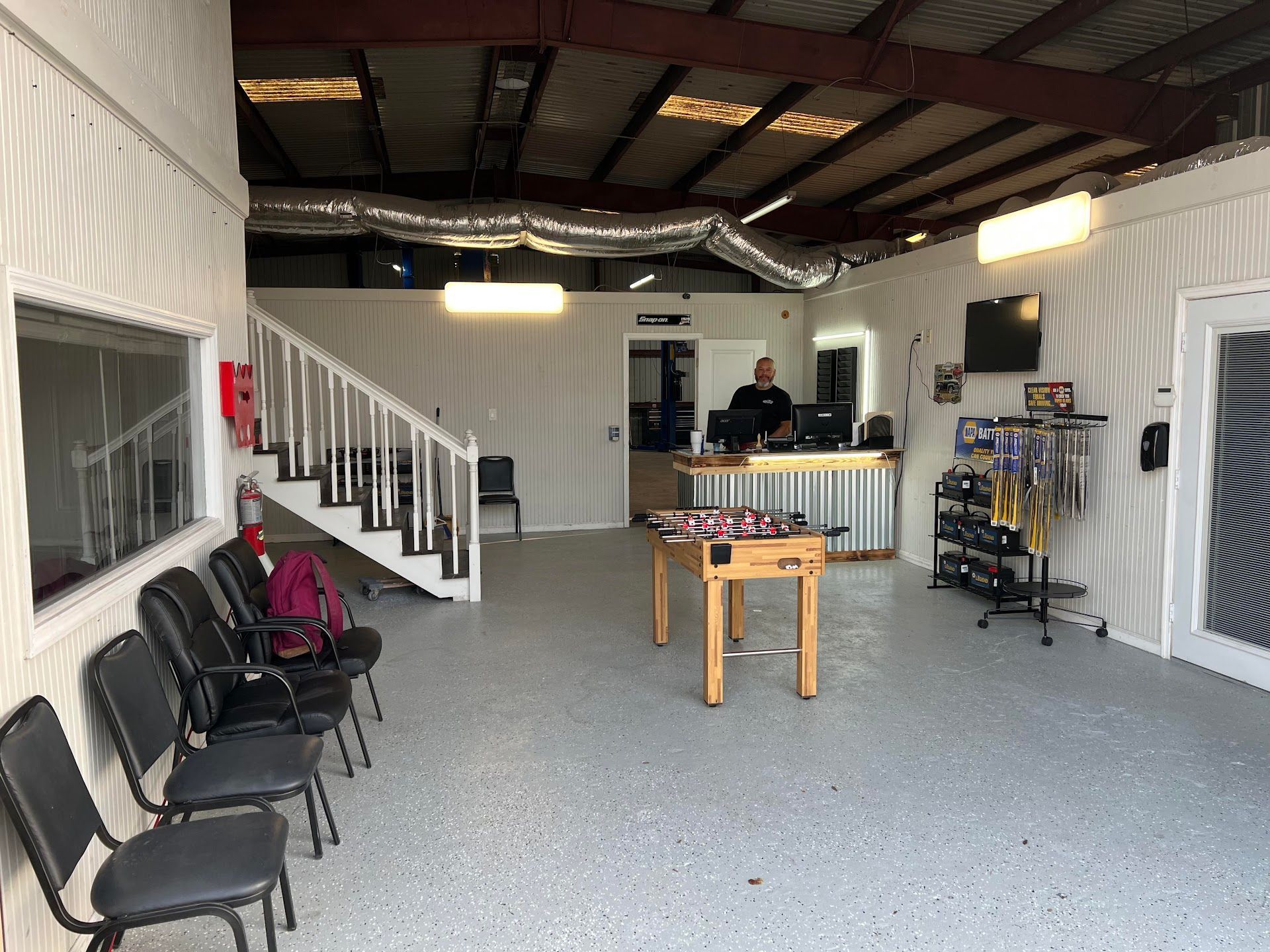 Interior of a waiting area with chairs, stairs, foosball table, and a person behind a counter. | CarDi Automotive