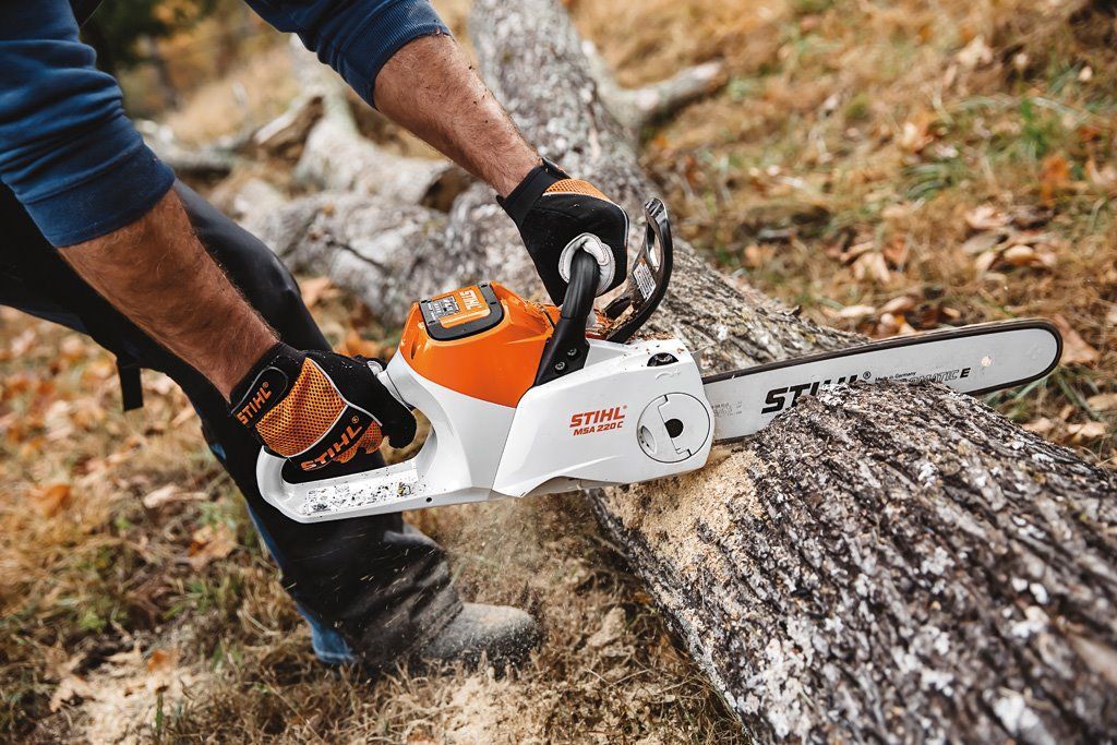Person Using A White And Orange Chainsaw To Cut A Log Outdoors — Stihl Shop Atherton In Mareeba, QLD