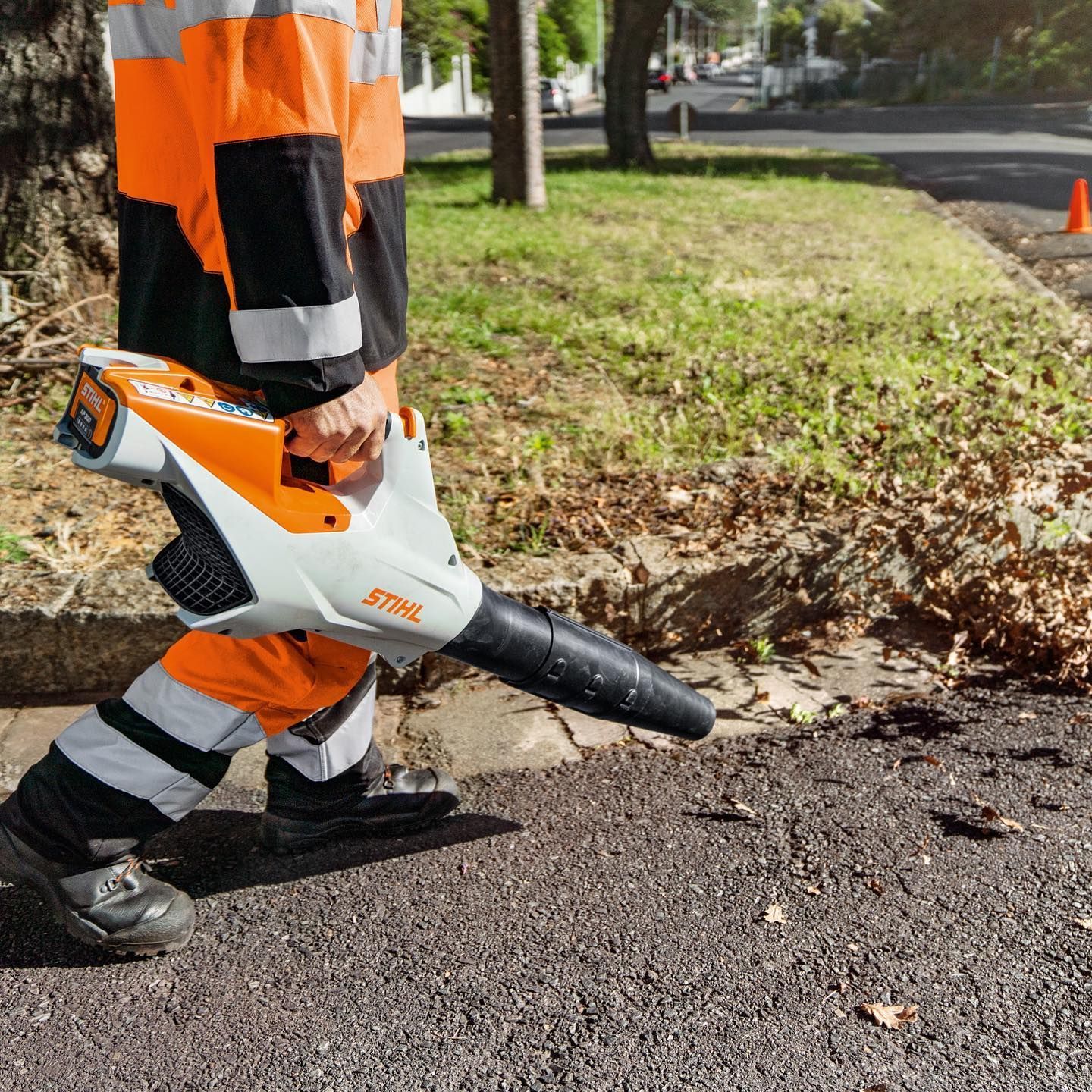 Worker In Orange And Black Vest Uses A Stihl Leaf Blower — Stihl Shop Atherton In Atherton, QLD