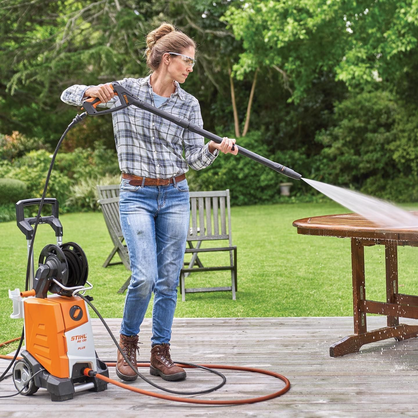 Woman Using A Pressure Washer On A Wooden Table Outdoors. Sunny Day, Green Background — Stihl Shop Atherton In Atherton, QLD