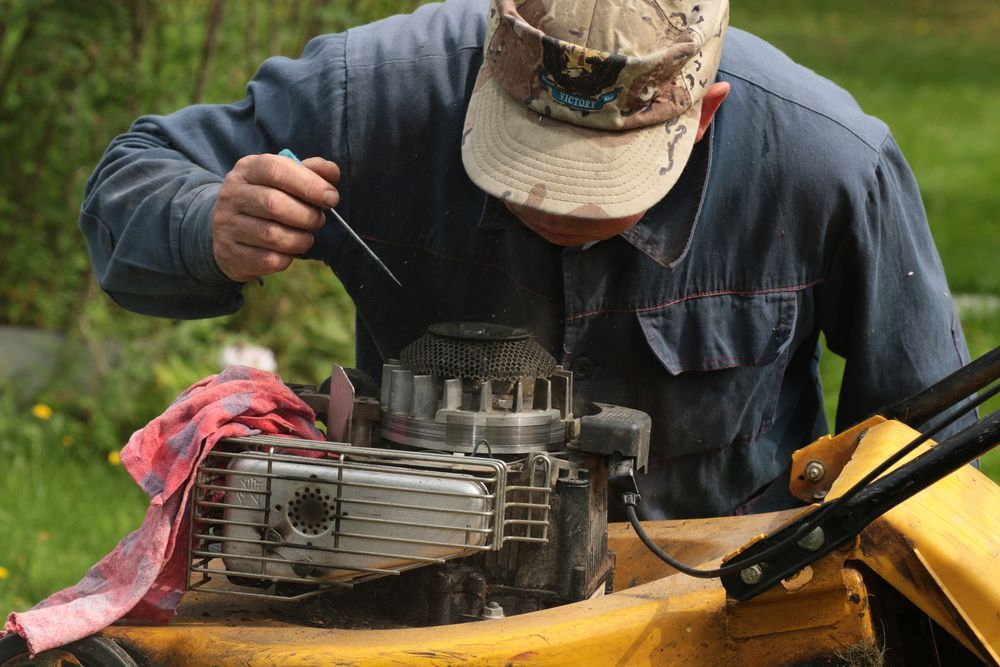 Man In Cap Working On A Lawnmower Engine With A Screwdriver — Stihl Shop Atherton In Mareeba, QLD