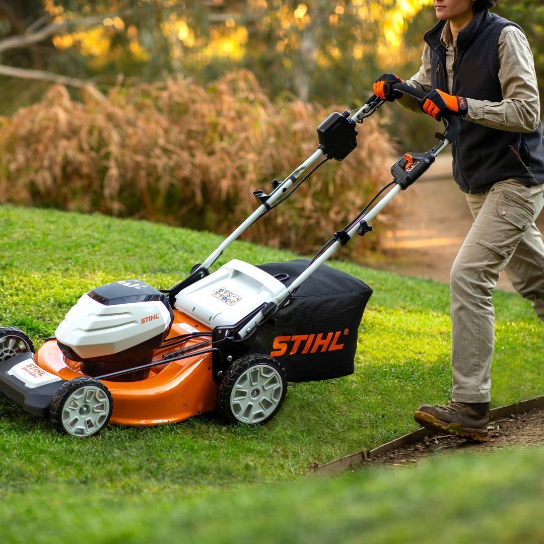 Woman Pushing An Orange And White Lawnmower Across Grass. Black Bag Attached — Stihl Shop Atherton In Atherton, QLD