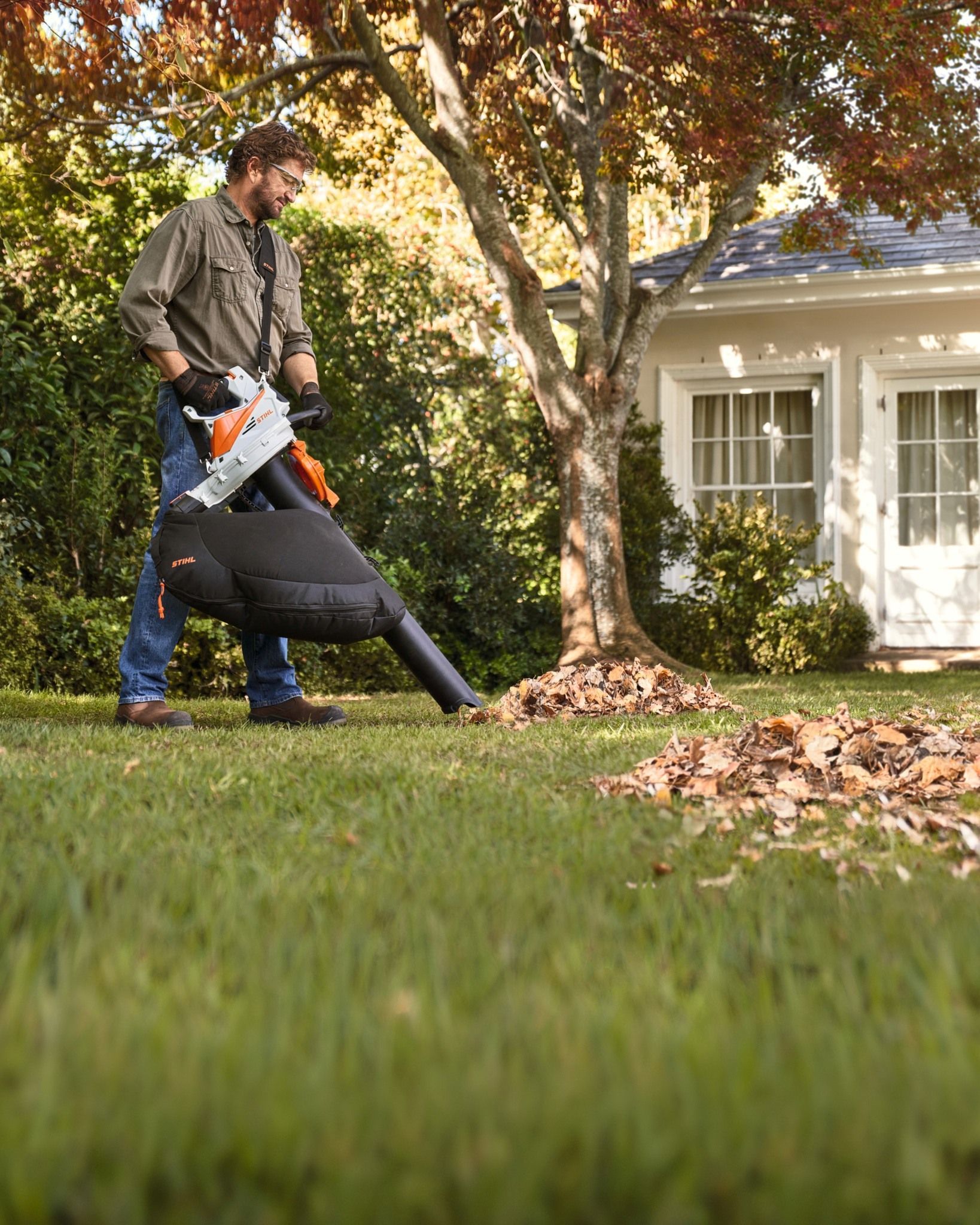Man Blowing Leaves On A Lawn With A Leaf Blower Near A Tree And House — Stihl Shop Atherton In Atherton, QLD