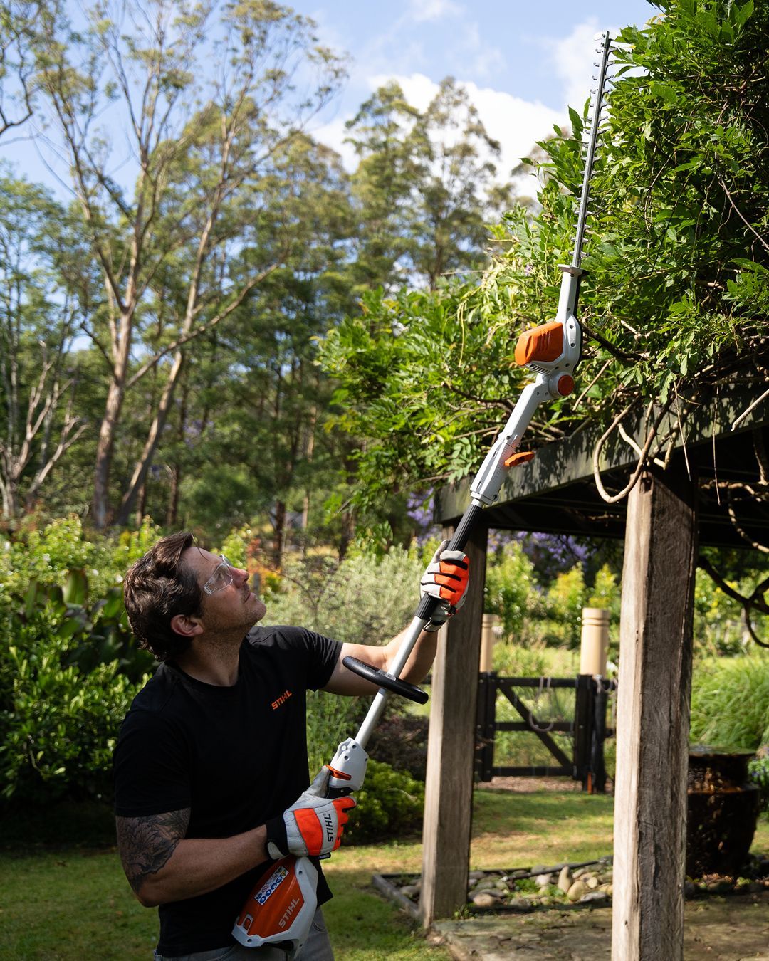 Man Mowing A Lawn With An Orange And White Electric Lawnmower In A Grassy Yard — Stihl Shop Atherton In Atherton, QLD
