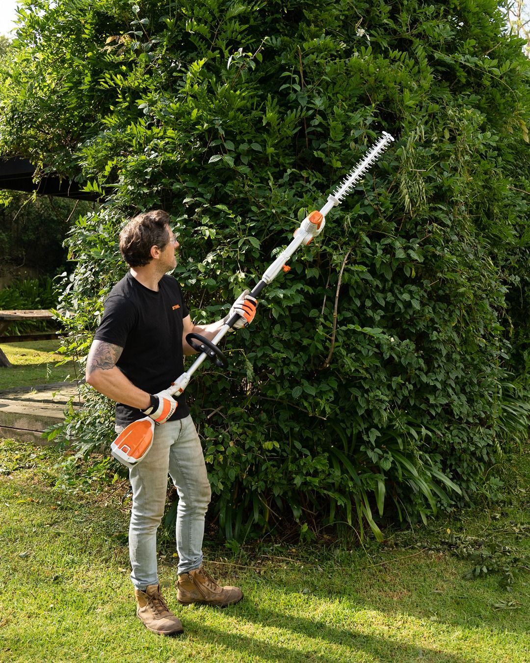 Man Trimming A Tall Hedge With A Long-reach Hedge Trimmer In A Garden — Stihl Shop Atherton In Atherton, QLD
