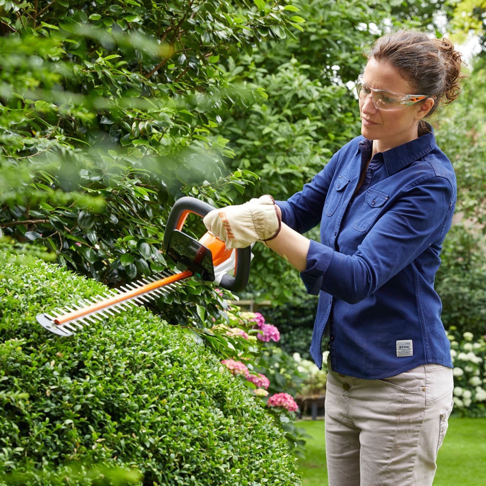 Woman Using Hedge Trimmer To Trim Bushes In A Garden — Stihl Shop Atherton In Atherton, QLD