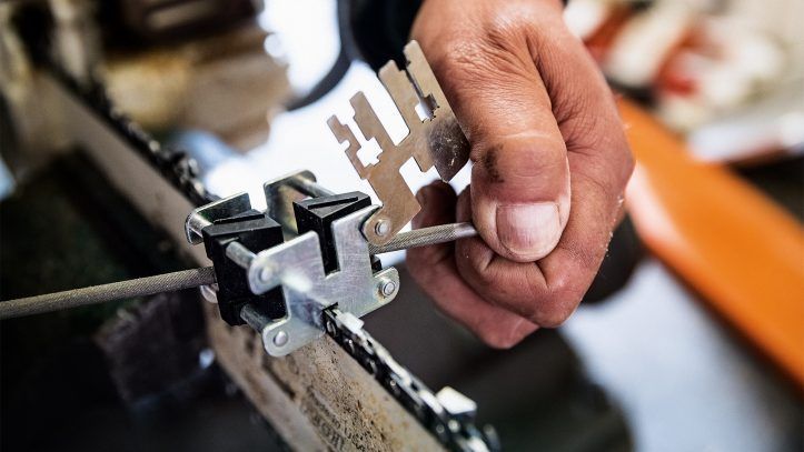 A hand uses a metal guide tool to sharpen a chainsaw blade with a file.— Stihl Shop Atherton In Atherton, QLD