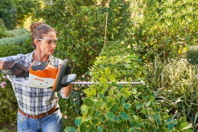 Person trimming hedges with a hedge trimmer in a lush garden or backyard — Stihl Shop Atherton In Atherton, QLD
