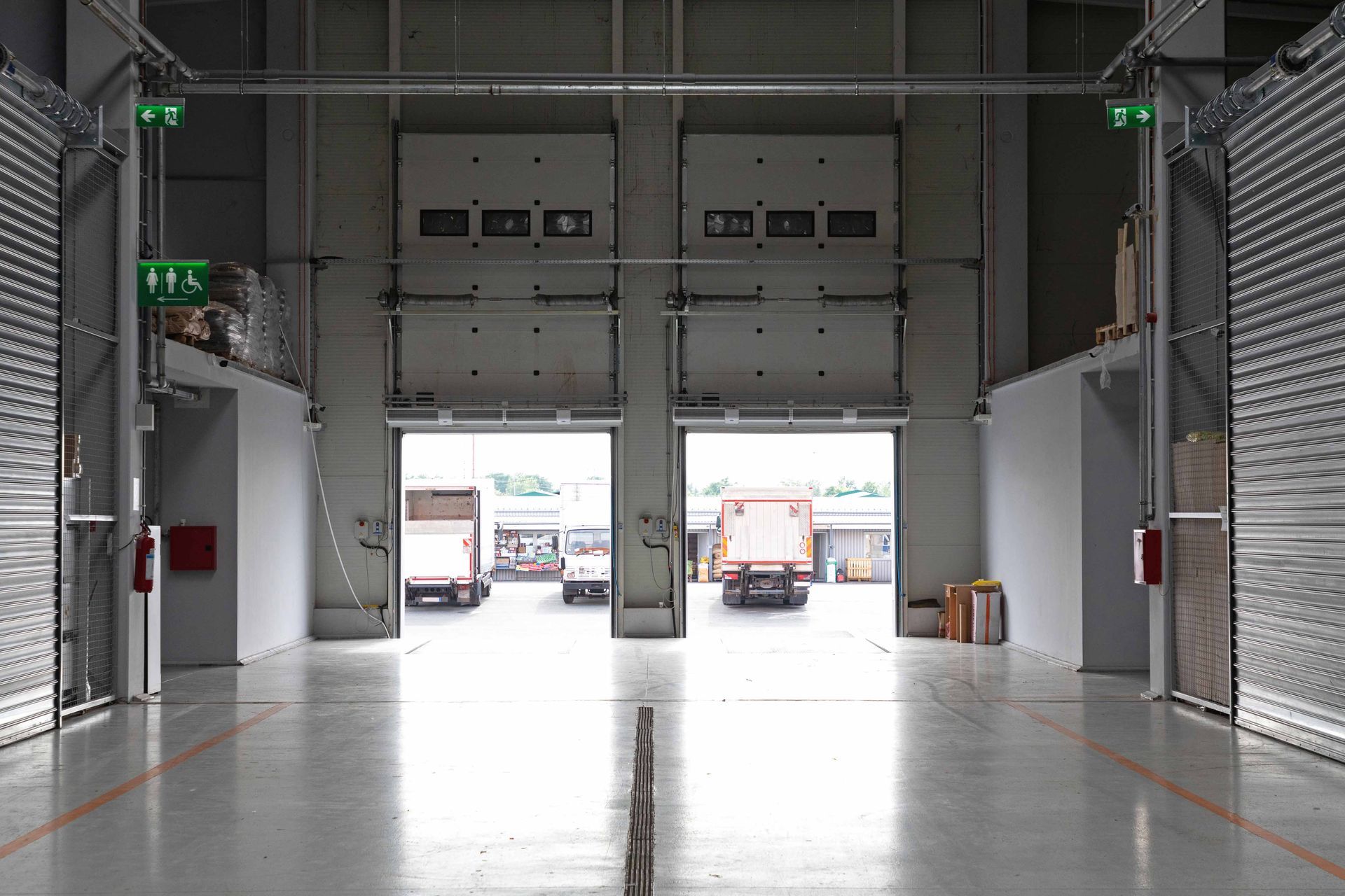 Interior of a warehouse with two open loading dock doors, roll-up doors and exit signs. 