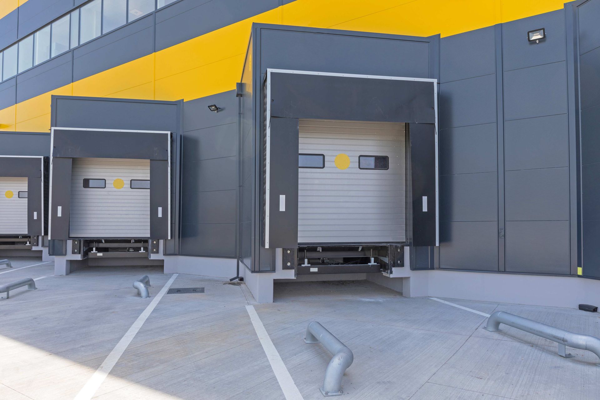 Three loading dock bays with closed roll-up doors on a modern industrial warehouse facade.
