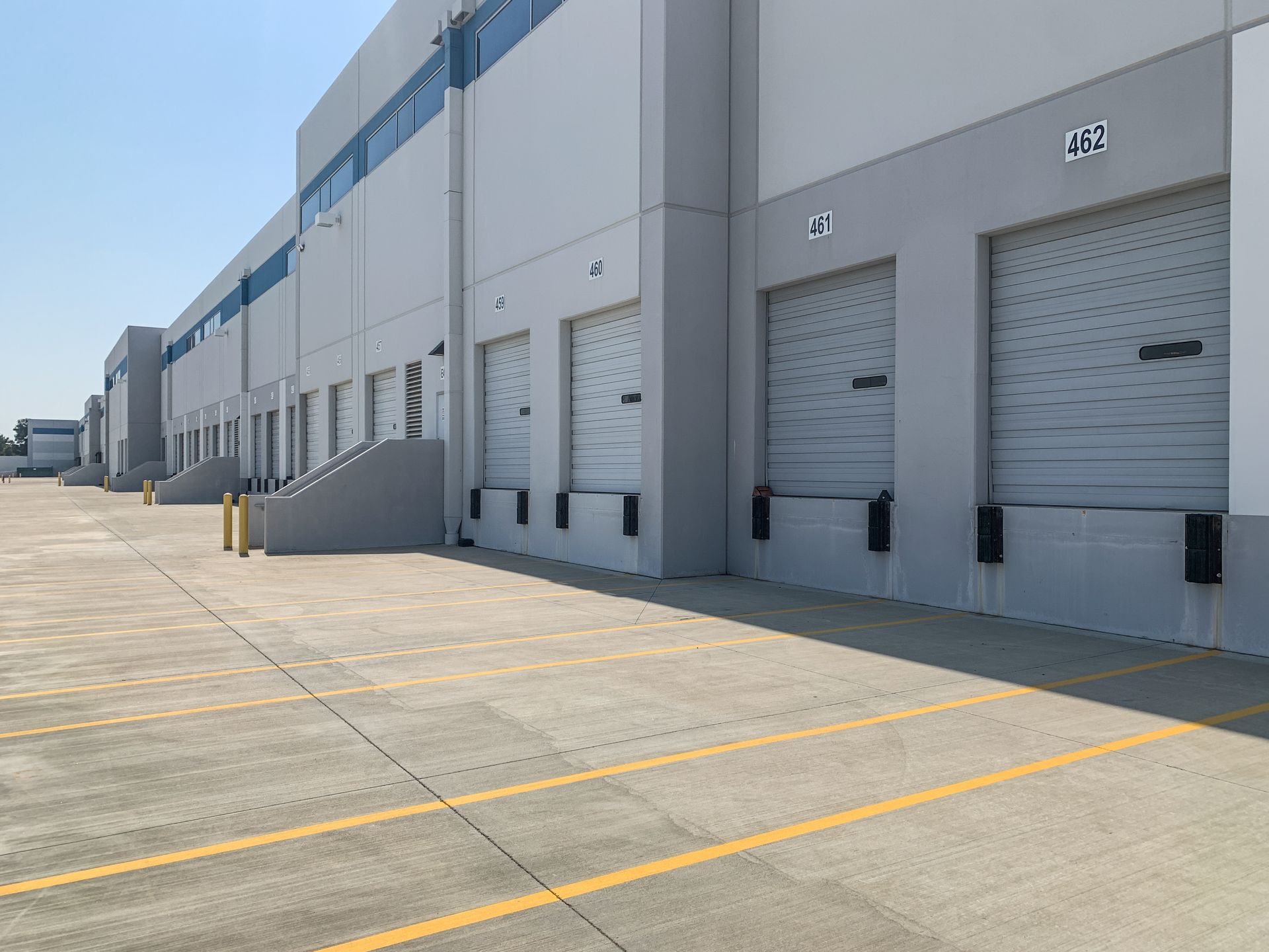 Industrial warehouse loading docks with gray roll-up doors and a wide concrete lot with yellow lines