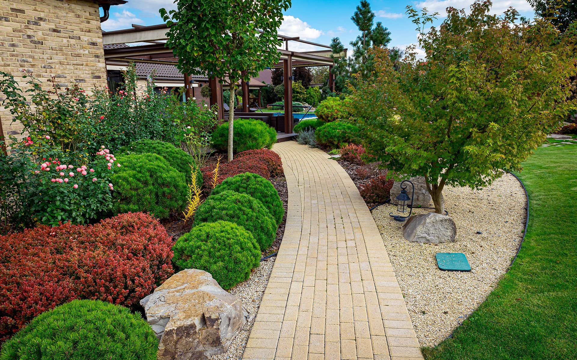 A brick walkway leading to a house in a lush green garden.