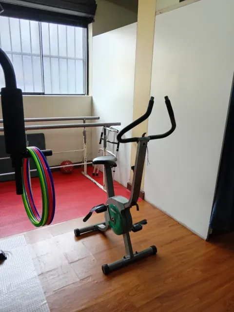 Habitación con una bicicleta estática, bandas de resistencia y una ventana junto a la pared.