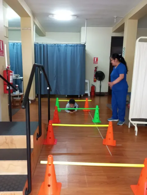 Un niño gatea por un circuito de obstáculos colorido en un gimnasio mientras un miembro del personal lo observa cerca