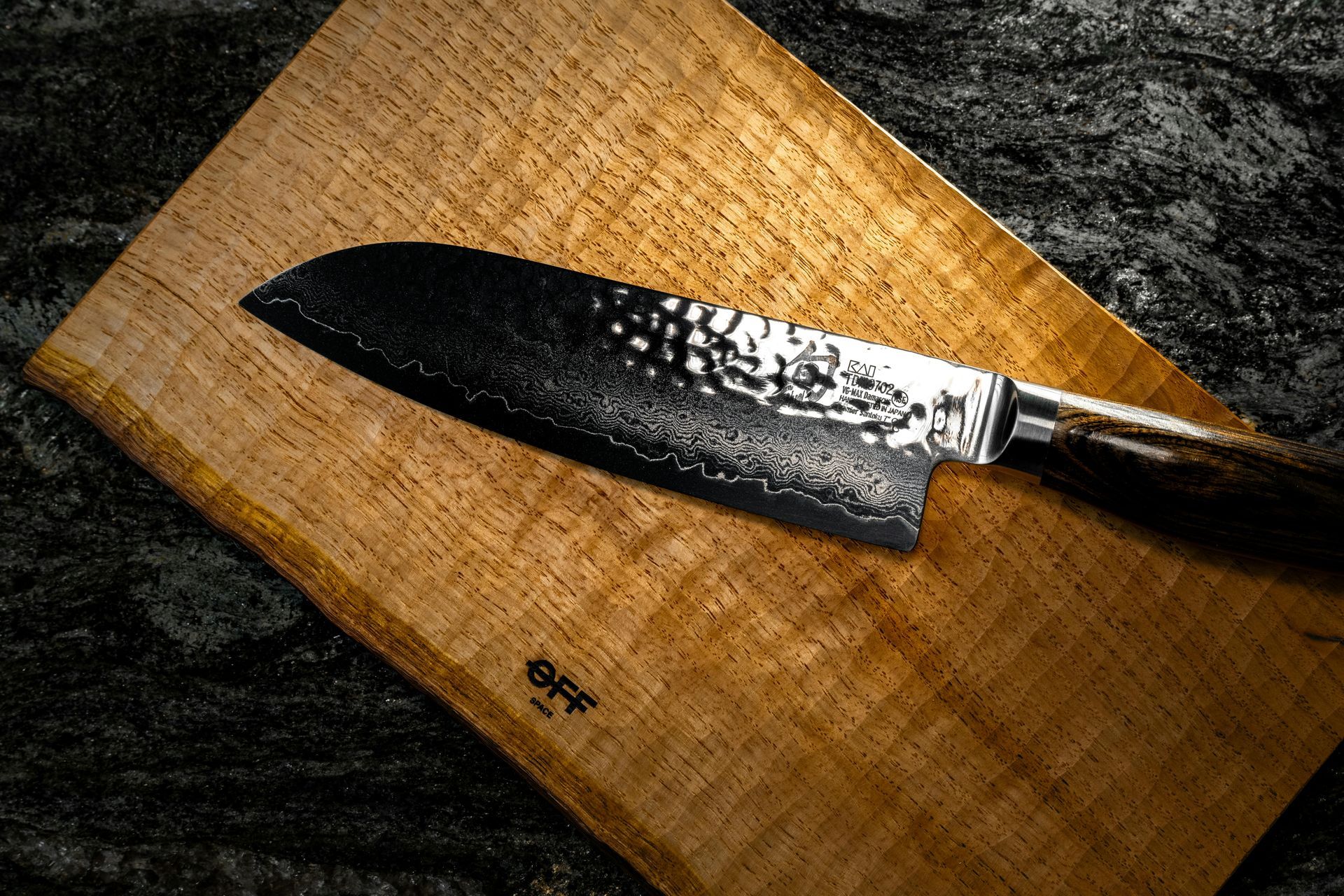 Black chef’s knife on a wooden cutting board with a dark stone background