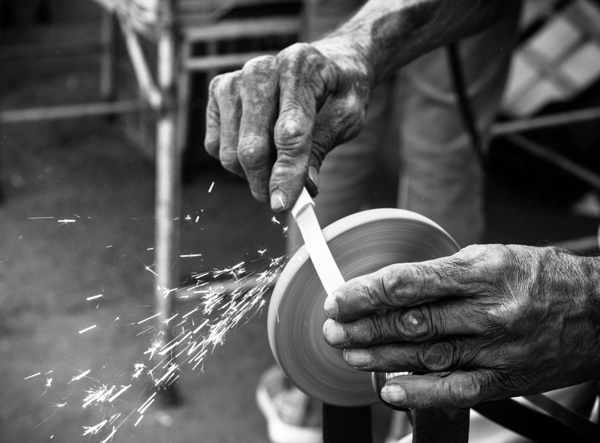 Hands grinding a bowl on a wheel, with sparks flying in a workshop.